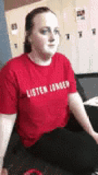 a woman wearing a red t-shirt is sitting on a bed .