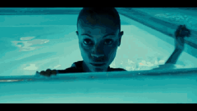 a woman is swimming in a pool with a blue light shining on her face