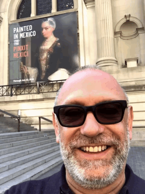 a bald man wearing sunglasses is smiling in front of a poster that says painted in mexico