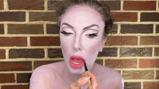 a woman with pink paint on her face has a tattoo of a heart on her finger