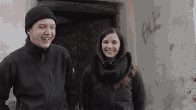 a man and a woman are smiling in front of a wall that has the word ple written on it