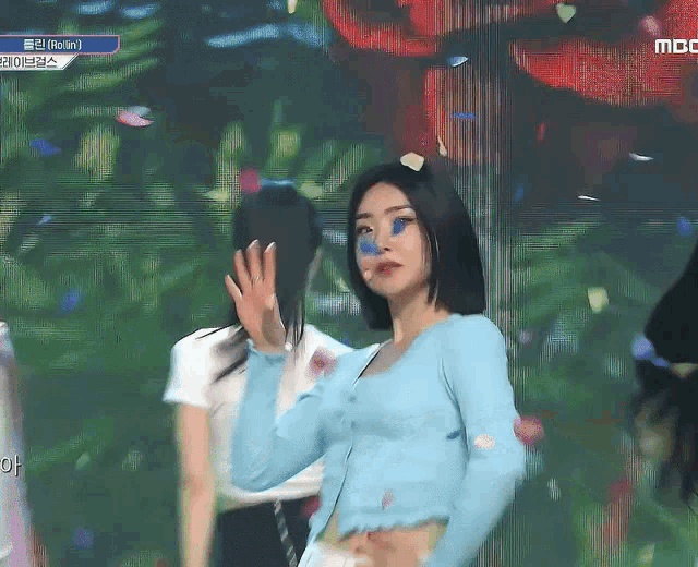a woman in a blue sweater stands on a stage in front of a screen that says mbc