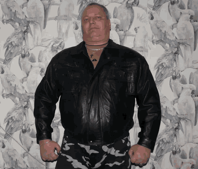 a man wearing a black leather jacket stands in front of a wall covered in birds