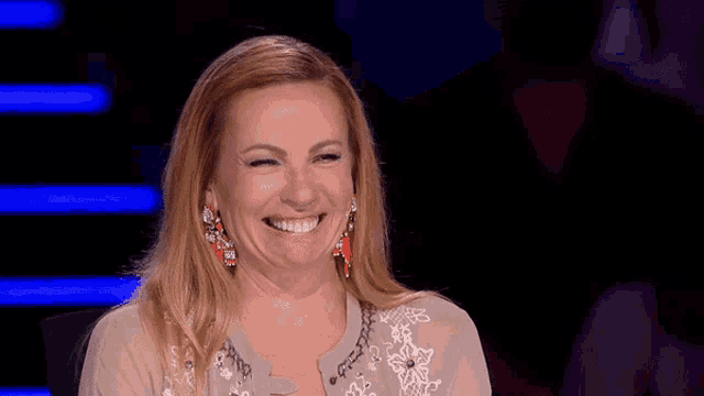 a woman wearing earrings is smiling and sitting in front of a dark background