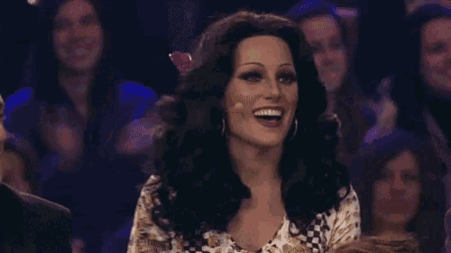 a woman wearing a wig is laughing in front of a crowd .