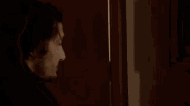 a man is standing in front of a door in a dark room and looking at the camera .