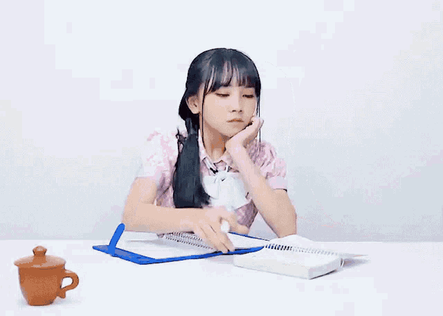 a girl is sitting at a desk with a book and a cup