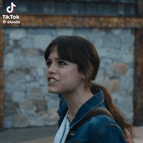 a woman in a denim jacket is screaming in front of a stone wall with a tiktok watermark