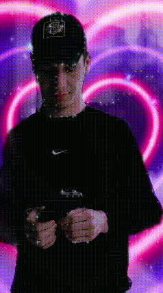 a man wearing a hat and a black shirt is holding a cell phone in front of a heart shaped background .