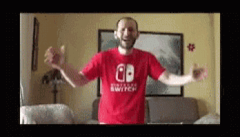a man wearing a red nintendo switch shirt is dancing in a living room
