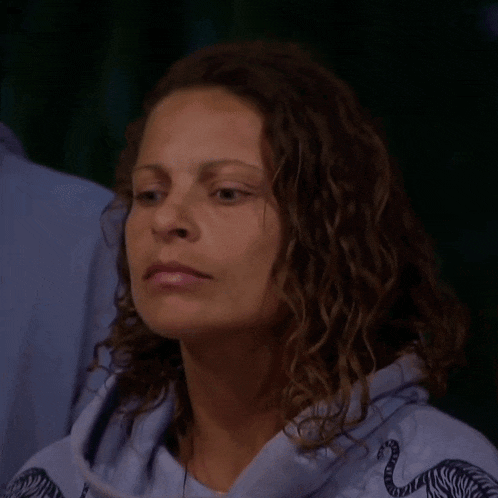 a woman with curly hair is making a funny face while wearing a blue shirt .