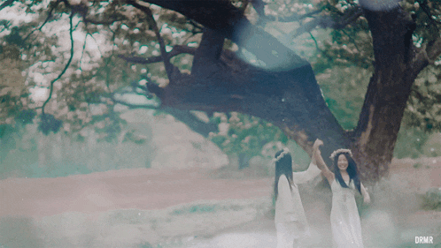two women standing under a tree with drmr on the bottom