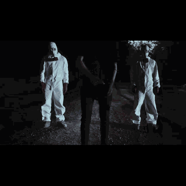 a man in a gas mask stands next to two other men in white suits
