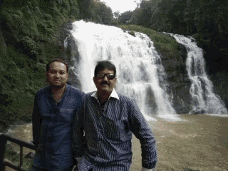 two men pose in front of a waterfall