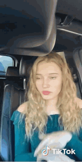 a woman is sitting in the back seat of a car with a tiktok logo on the bottom right corner .