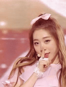 a woman is holding her finger to her lips while wearing a pink shirt .