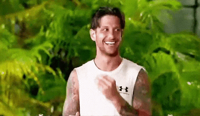 a man wearing a white under armour tank top is smiling and clapping .