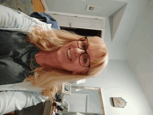 a woman wearing glasses and a gray shirt is smiling