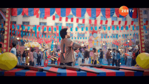 a man stands in front of a crowd at a carnival with a zee tv logo in the corner