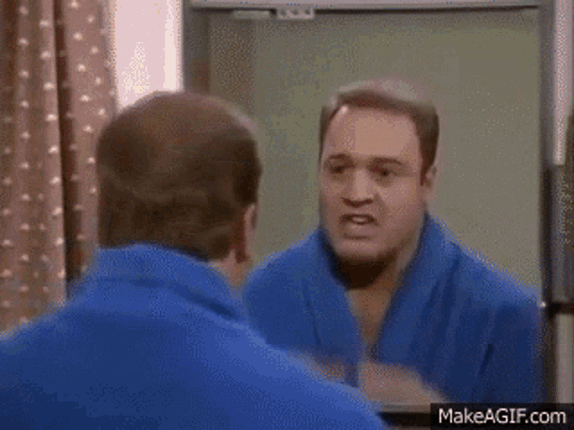 a man in a blue robe is looking at his face in the mirror .