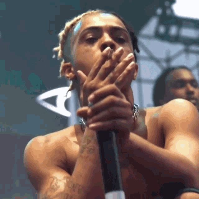 a man without a shirt is singing into a microphone while covering his mouth with his hands