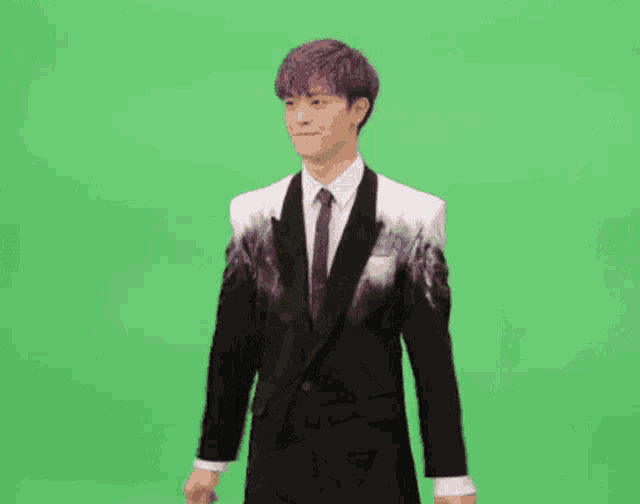a man in a suit and tie is dancing in front of a green background