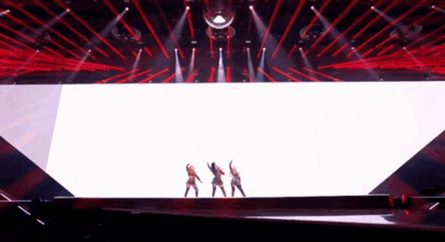 a group of people are dancing on a stage with red lights