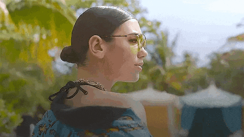 a woman wearing sunglasses and a bun looks over her shoulder .