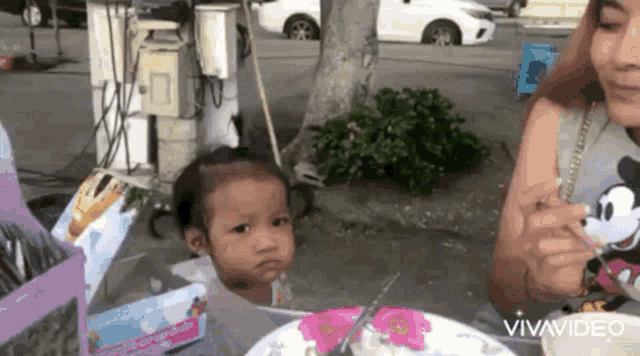 a little girl is sitting at a table next to a woman eating food .