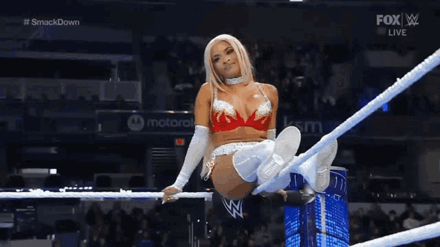 a woman is sitting on a rope in a wrestling ring with her feet up .