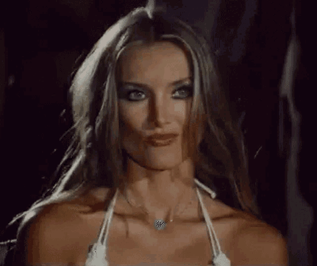 a woman in a white bikini top and necklace is making a face .