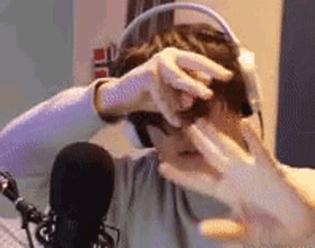 a man wearing headphones is sitting in front of a microphone and covering his face with his hands .