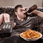 a man sitting on a couch drinking a beer and eating chips