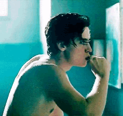 a man without a shirt is brushing his teeth in front of a mirror .
