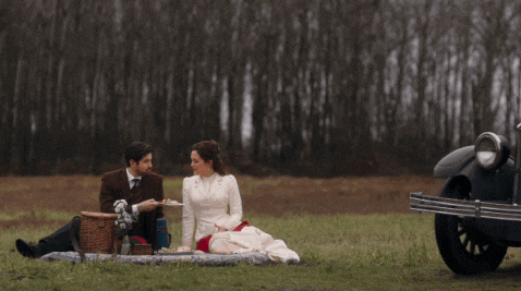 a man and woman are having a picnic in a field next to a car