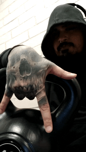 a man with a tattoo of a skull on his hand holds up his index finger