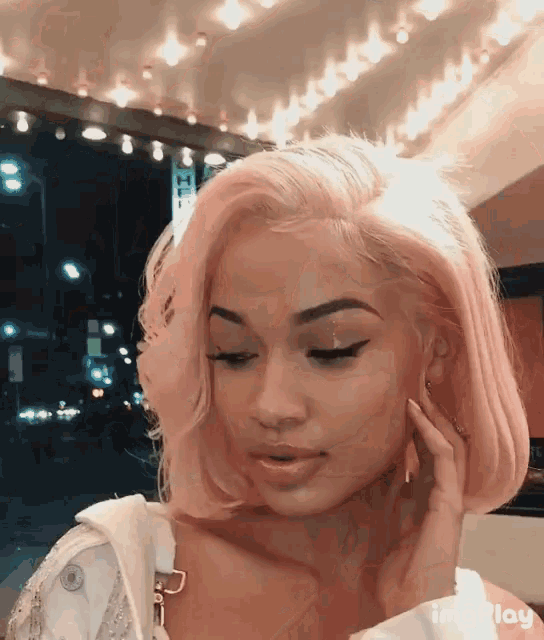 a woman with pink hair is looking at the camera while wearing a white jacket ..
