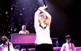 a woman is singing into a microphone on a stage with a piano in the background .