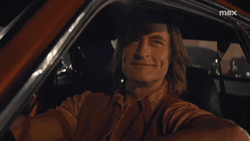 a man is taking a selfie in a car with a max logo in the corner