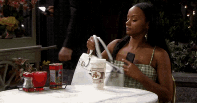 a woman is sitting at a table with a cup of coffee and a bag that says dj on it