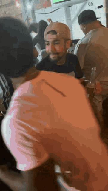a man wearing a baseball cap is talking to another man in a crowd of people .