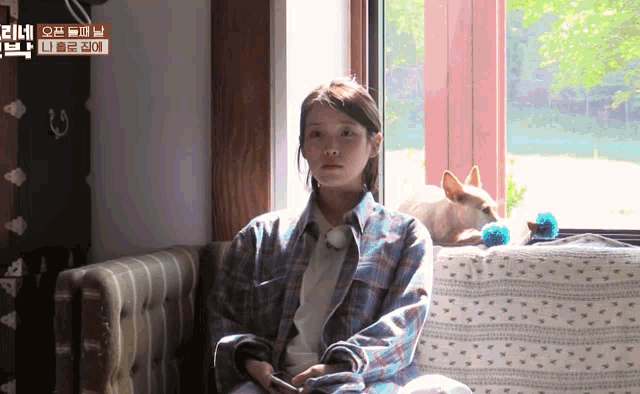 a woman sits on a couch next to a dog and a sign that says ' iu '