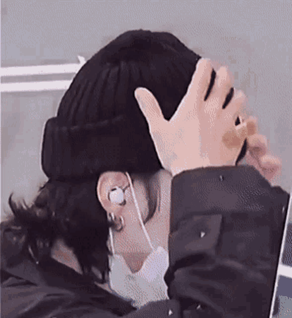 a person wearing a beanie and earbuds covering their face with their hand