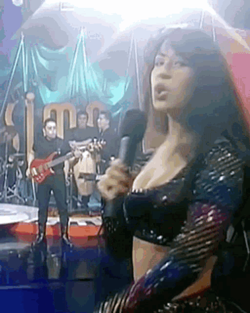 a woman is singing into a microphone on a stage with a band behind her .