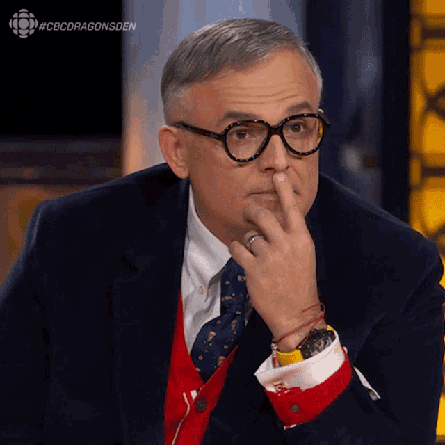 a man wearing glasses and a suit is sitting in front of a screen that says cbcdragonsden