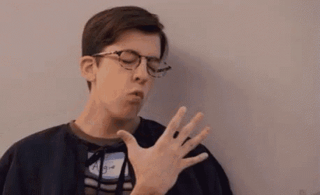 a young man wearing glasses is yawning with his mouth open and his hand out .
