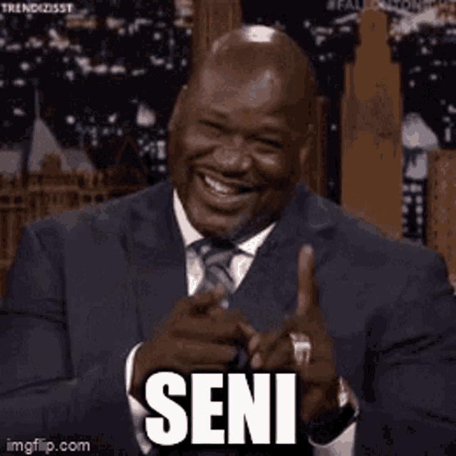 a man in a suit and tie is pointing at the camera with the word seni written on his face .