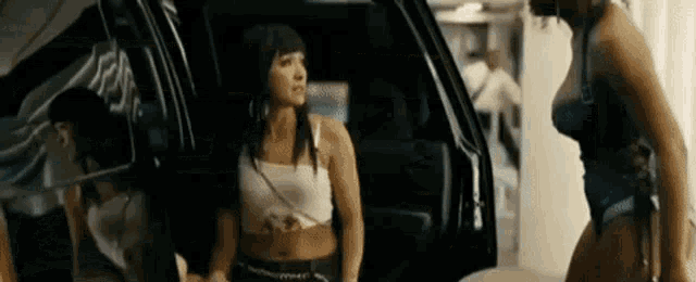 two women are standing next to each other in front of a car in a garage .