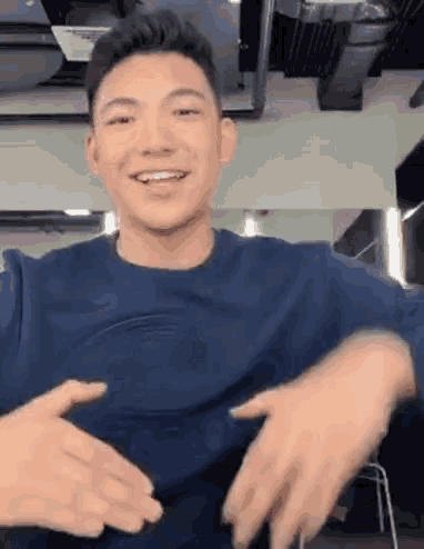 a young man in a blue shirt is making a funny face with his hands