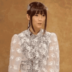 a woman wearing a white dress and earrings is standing in front of a wall .